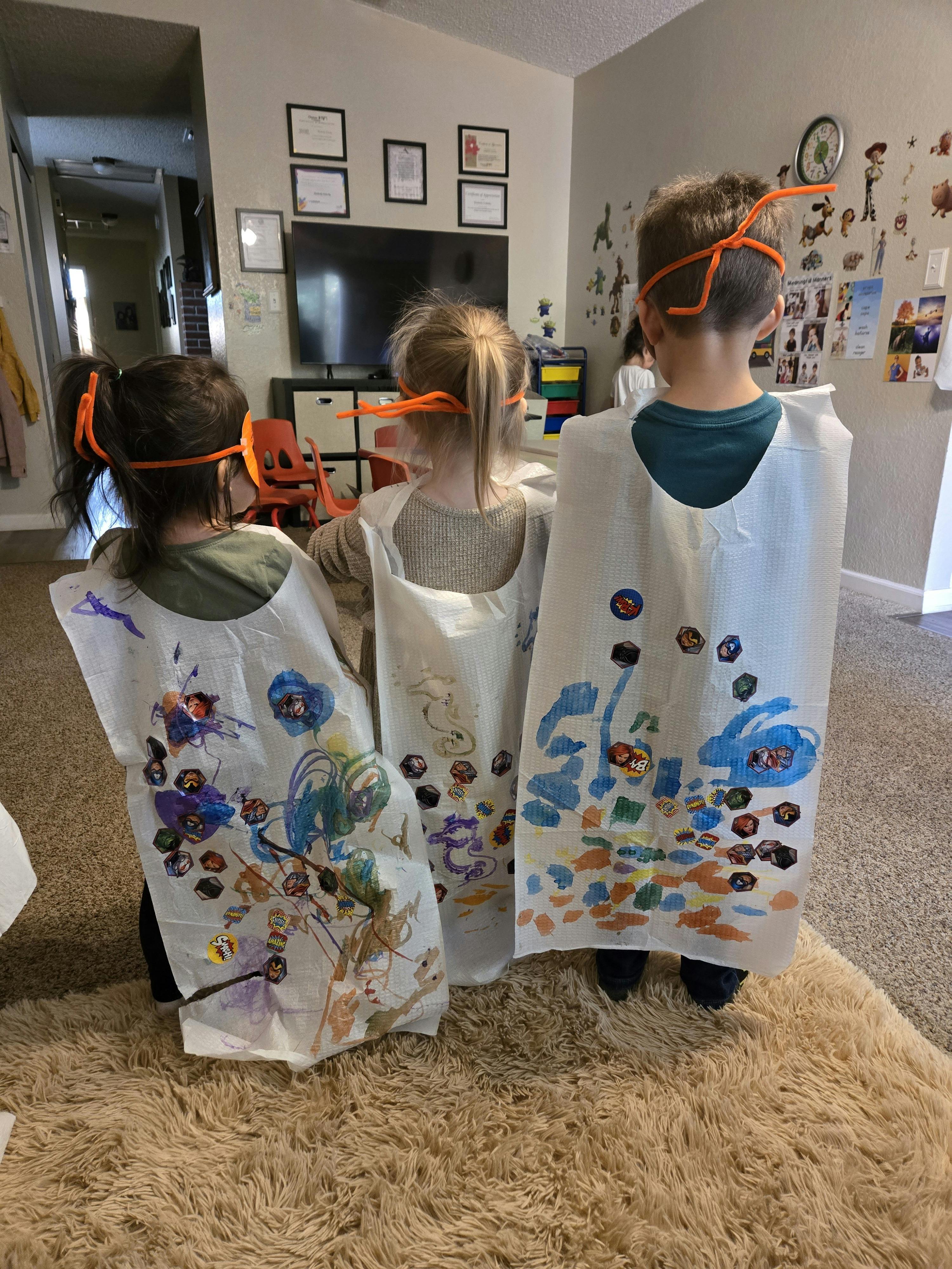 Three children wearing decorated smocks and orange headbands