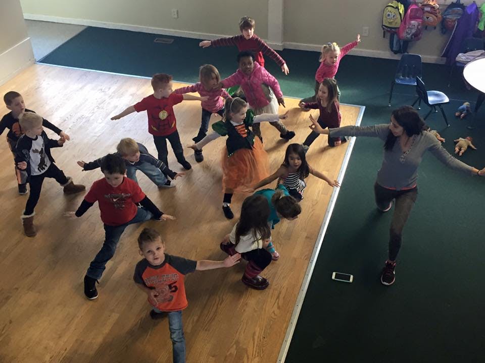 Adult and multiple children in a room with arms outstretched