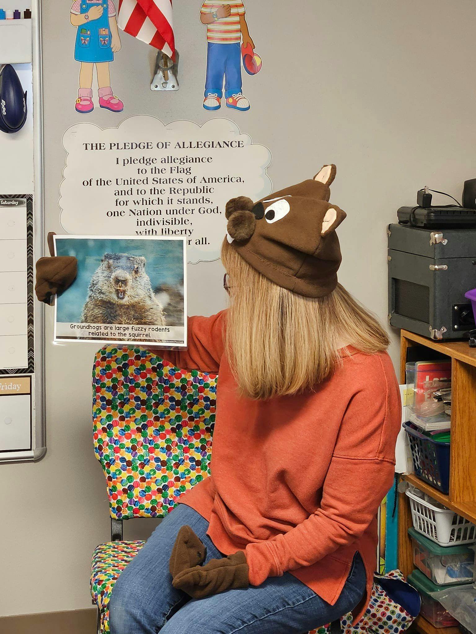 Person wearing a groundhog hat and gloves holding a picture of a groundhog