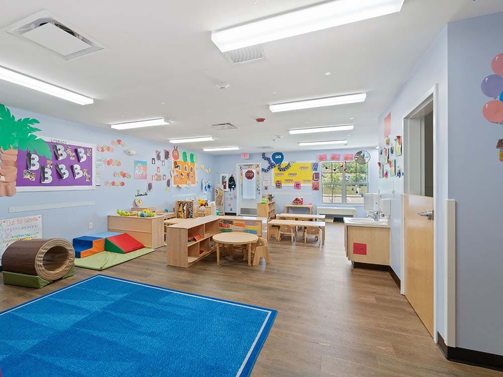 Empty classroom with colorful decorations, small tables, chairs, and play equipment