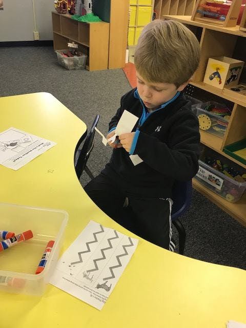 Child cutting paper with scissors at a yellow table