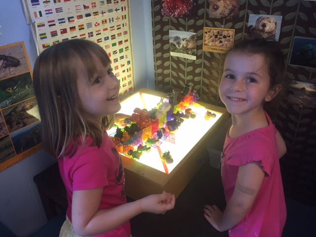 Two children standing by a light table with colorful objects