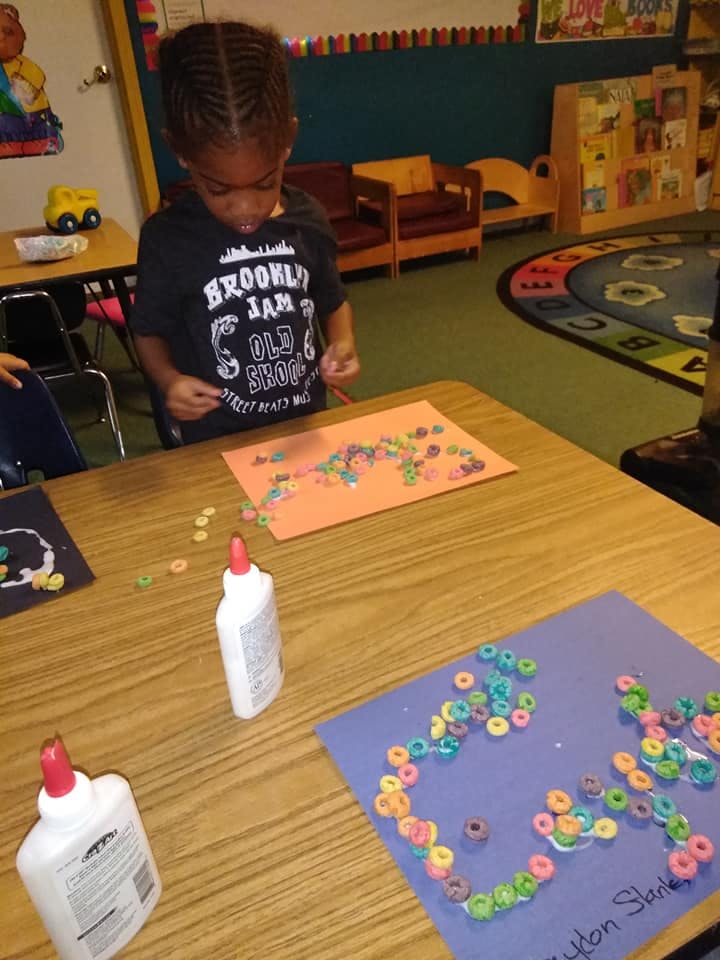 Child making art with cereal pieces and glue in a classroom