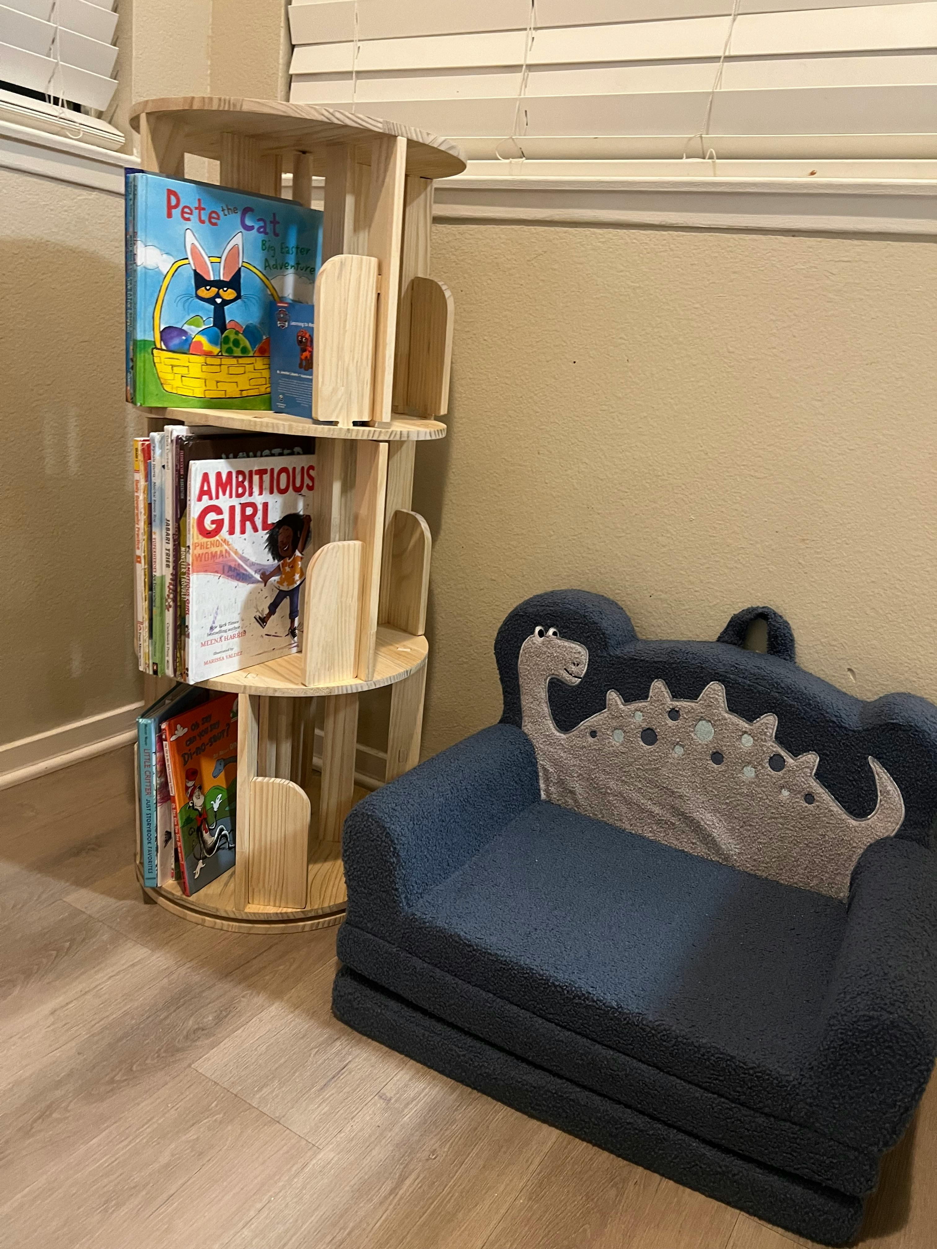 Wooden rotating bookshelf with books next to a blue child's sofa with a dinosaur