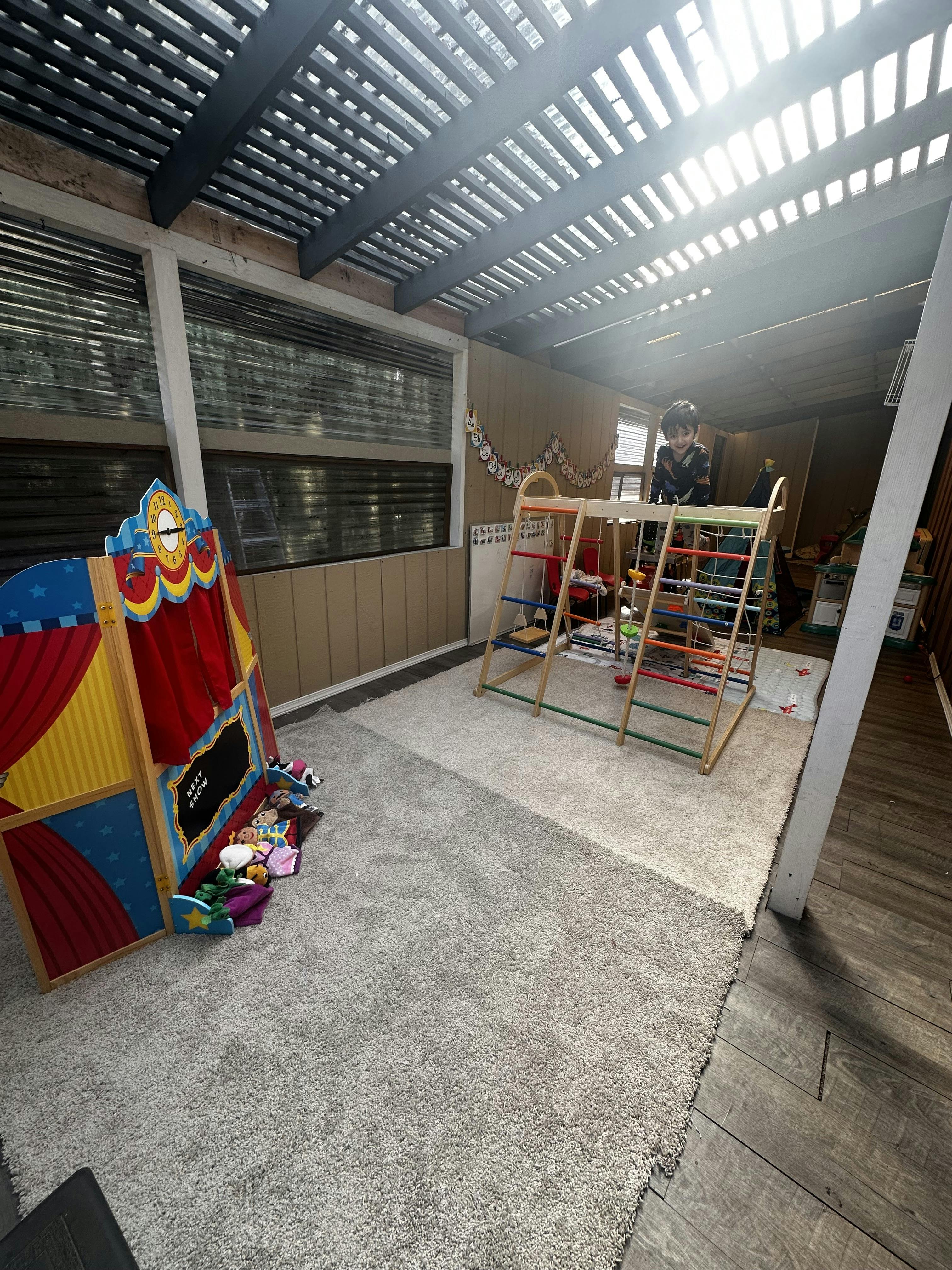 Child smiling at the top of a play climbing structure in a room with a puppet theater