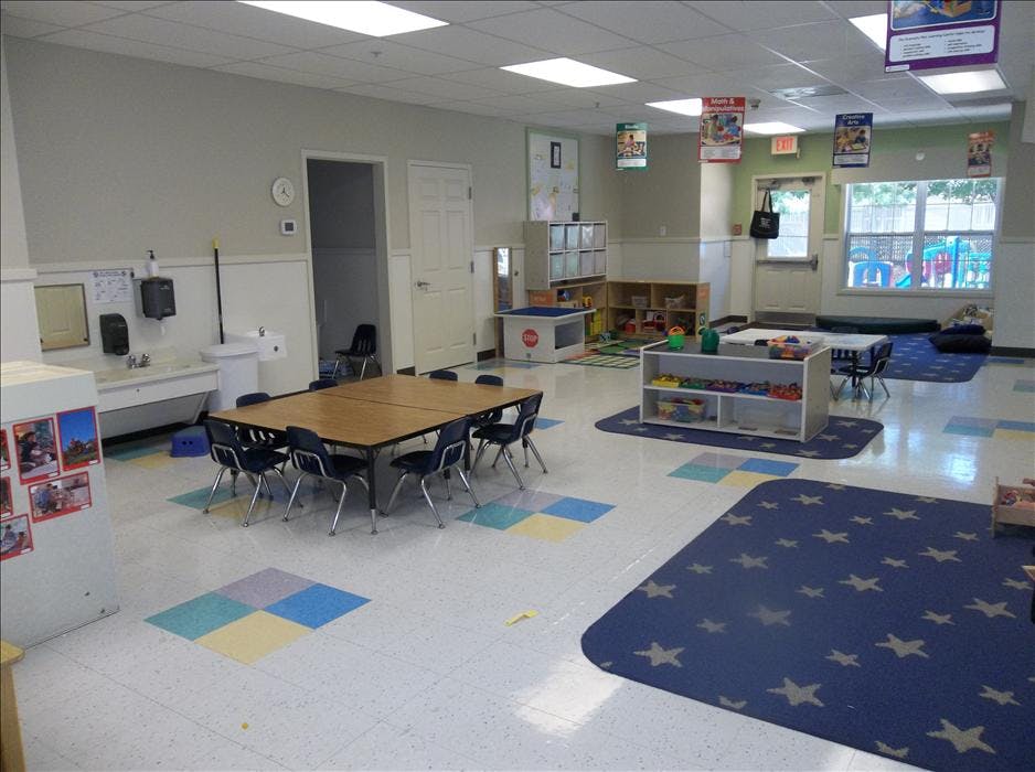 empty classroom with small tables and chairs, play mats, and toys