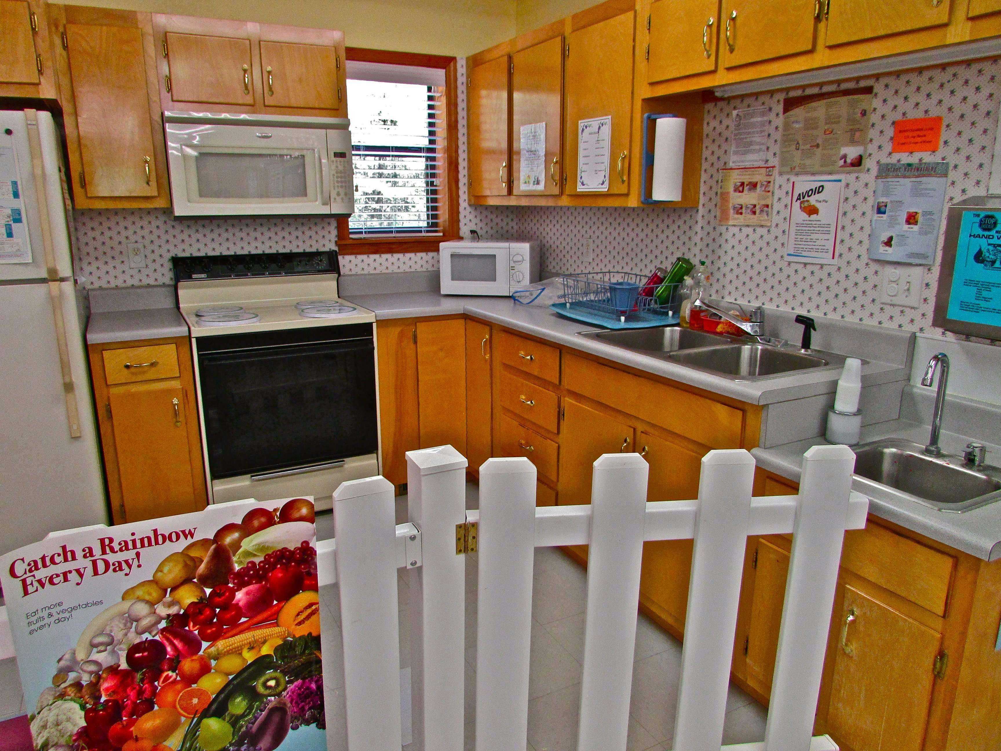 Kitchen with wooden cabinets, white appliances, and a white picket fence