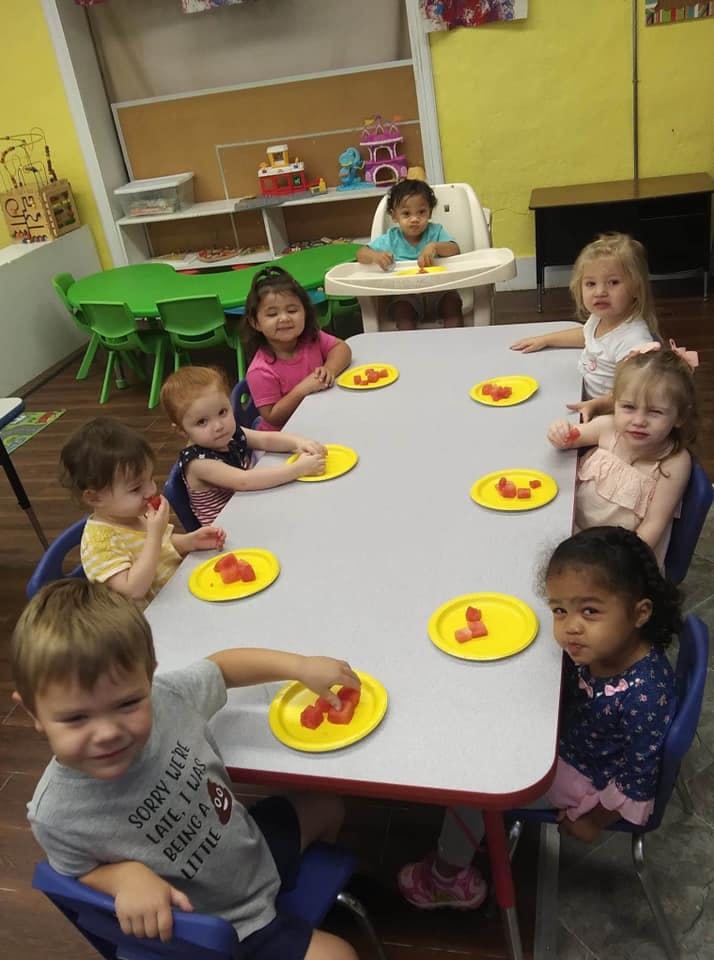 Children sitting at a table with plates of fruit