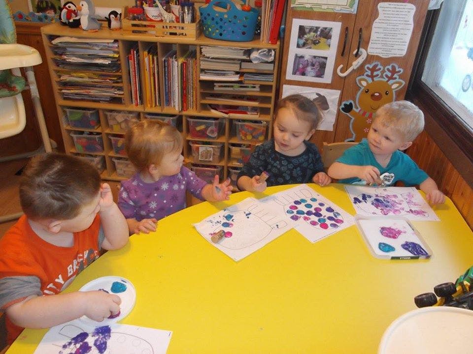Four children sitting at a yellow table doing crafts