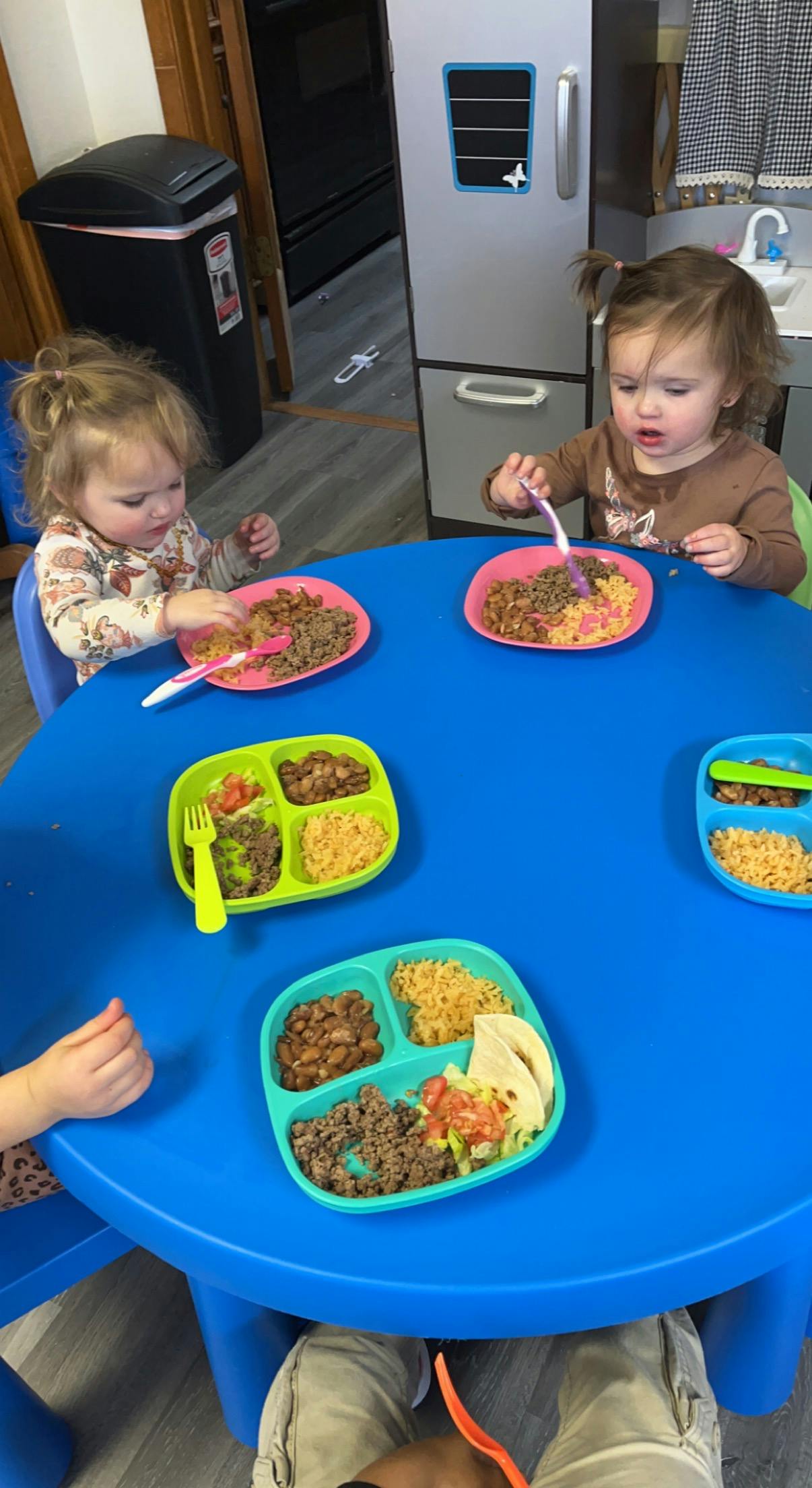 Two children eating at a blue table with divided plates of food