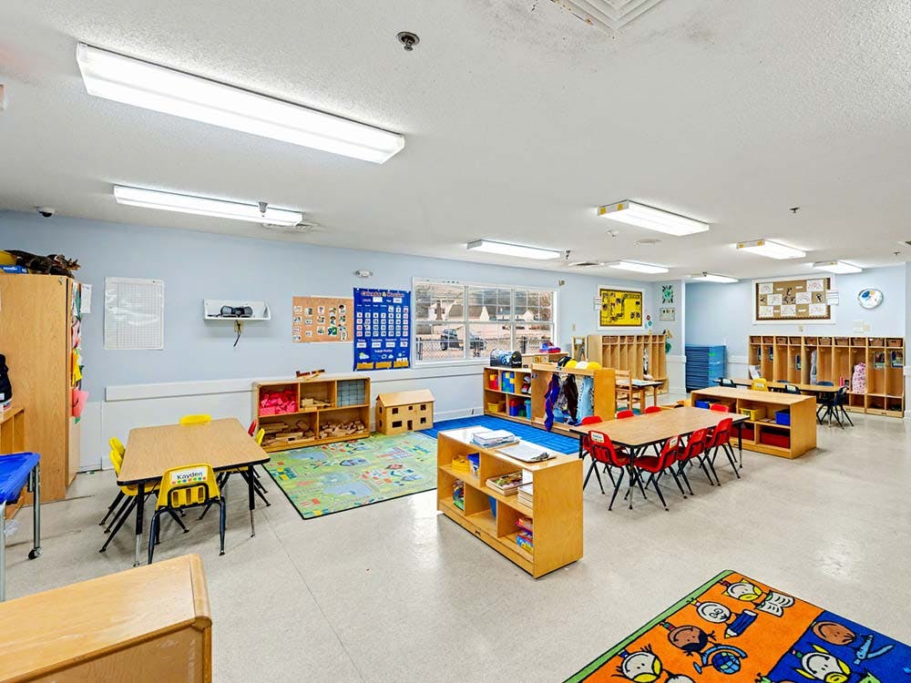 An empty classroom with small tables and chairs, shelves, and cubbies