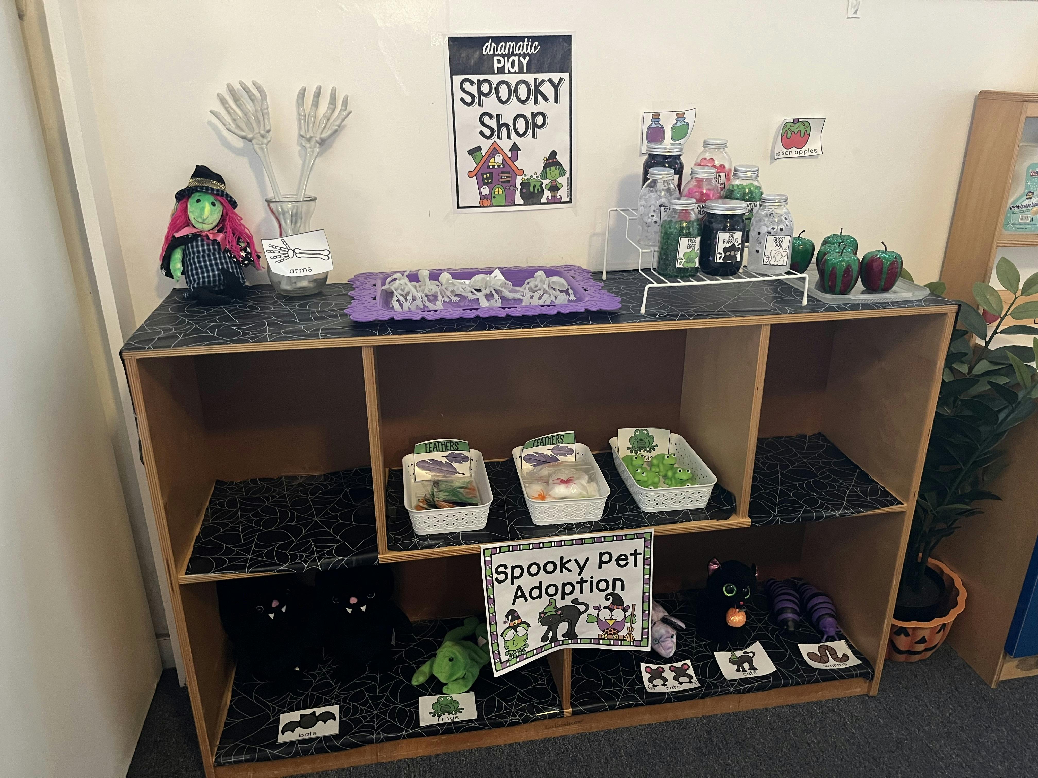 Halloween-themed display with a witch doll, skeleton hands, and "Spooky Shop" sign