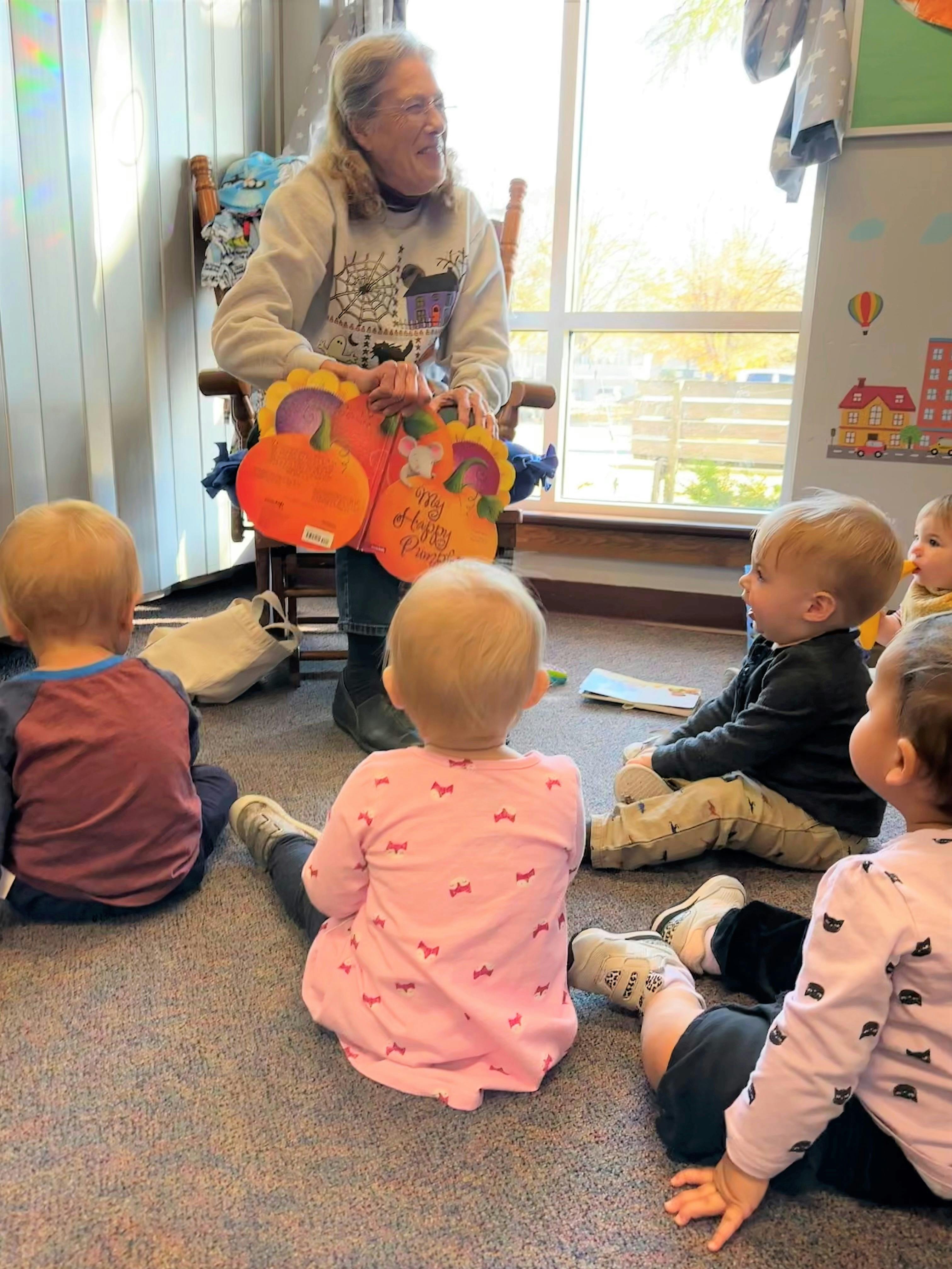 Person reading a pumpkin-shaped book to several children sitting on the floor