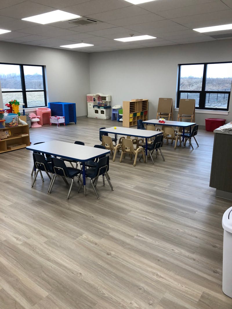 Classroom with small tables and chairs, play kitchen, and storage shelves