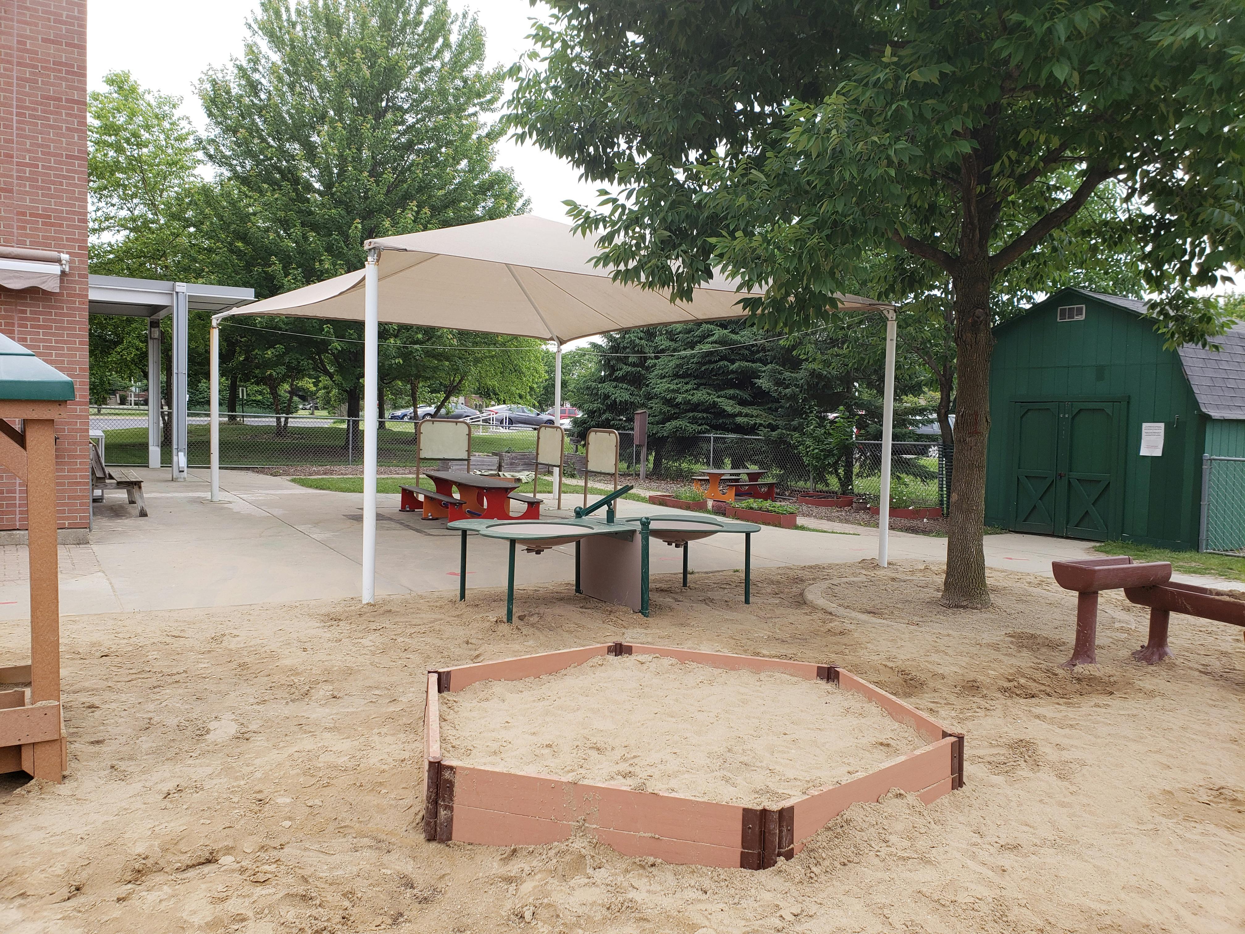 Outdoor playground with sandbox, tables, and shade structure