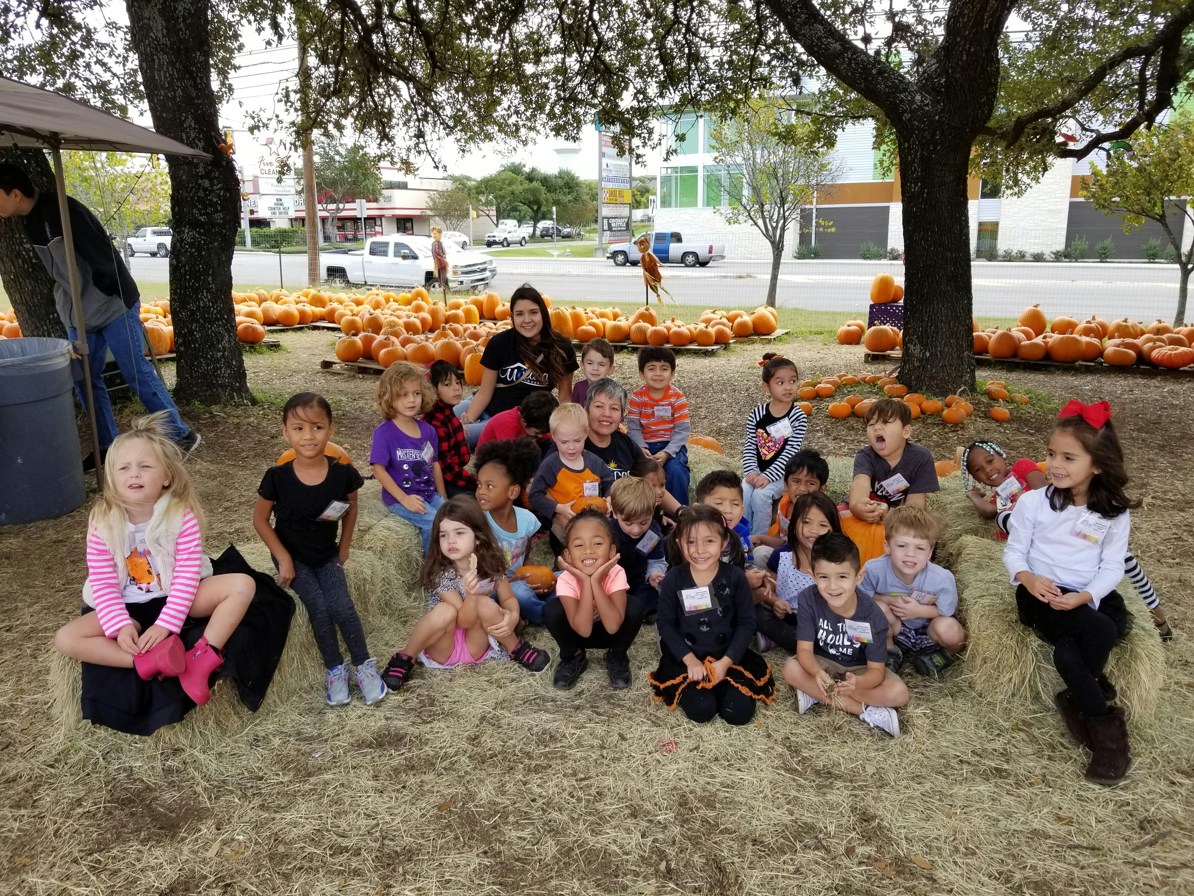 Adults and children sitting on hay bales in a pumpkin patch