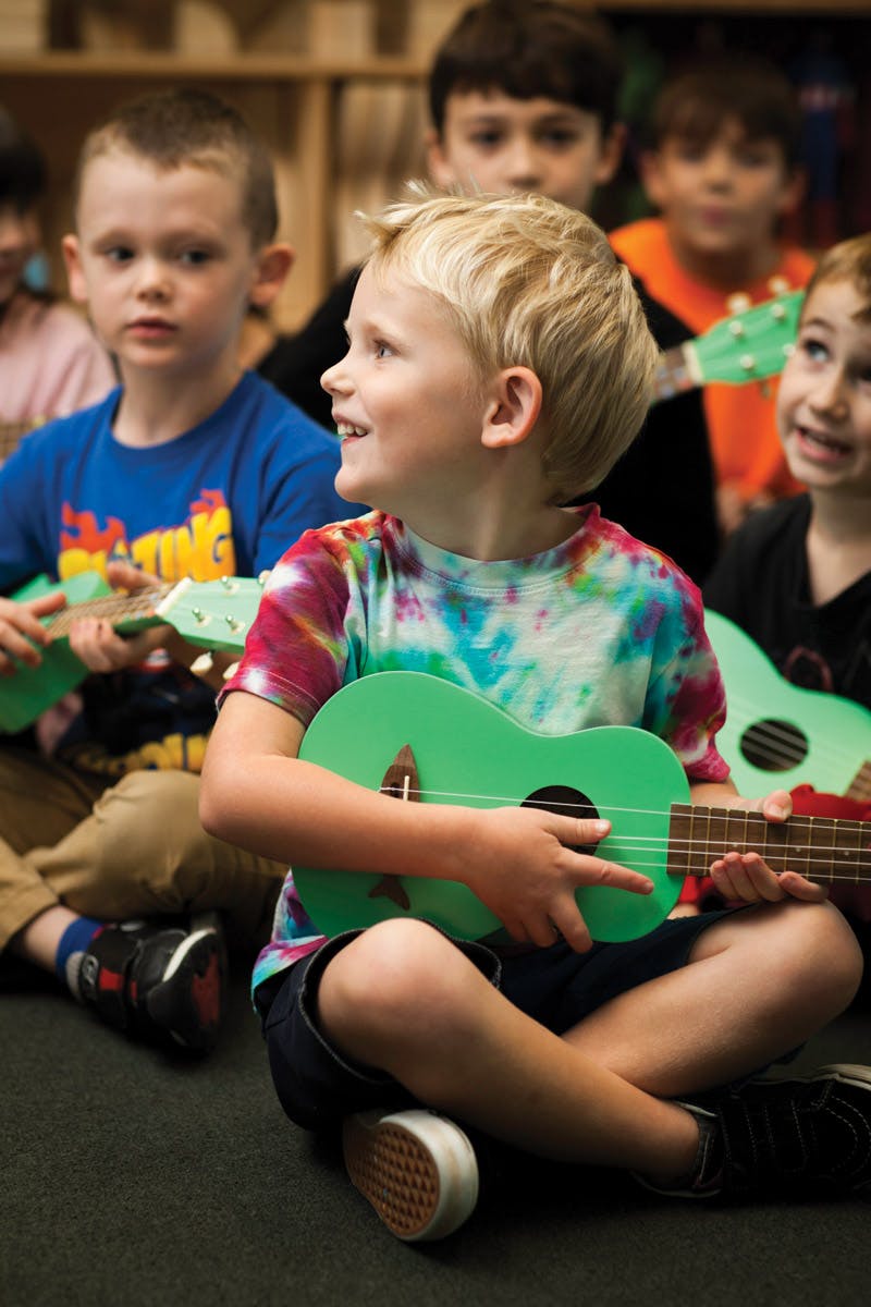 Children sitting on the floor playing green ukuleles