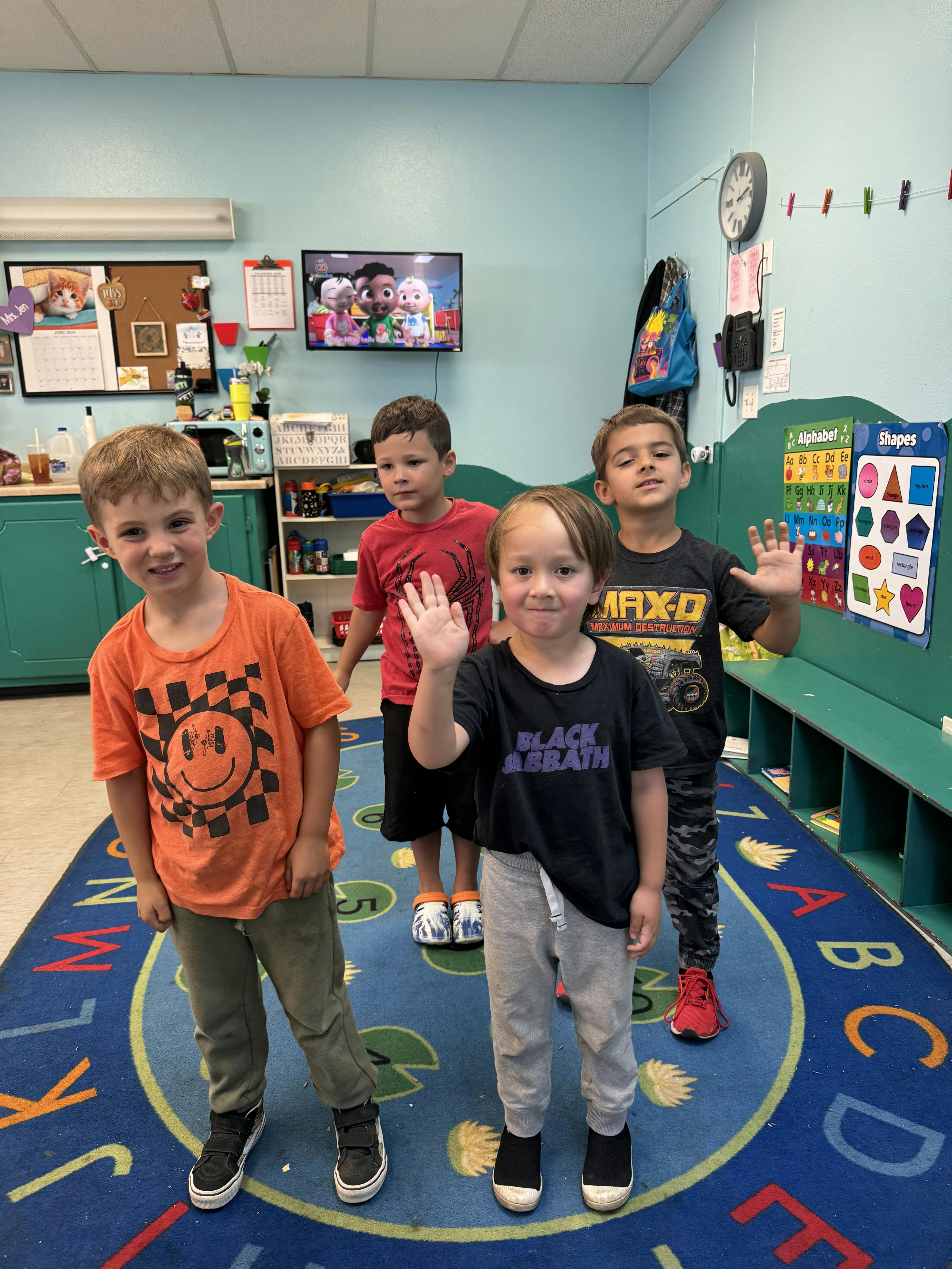Four children standing on a rug, two waving
