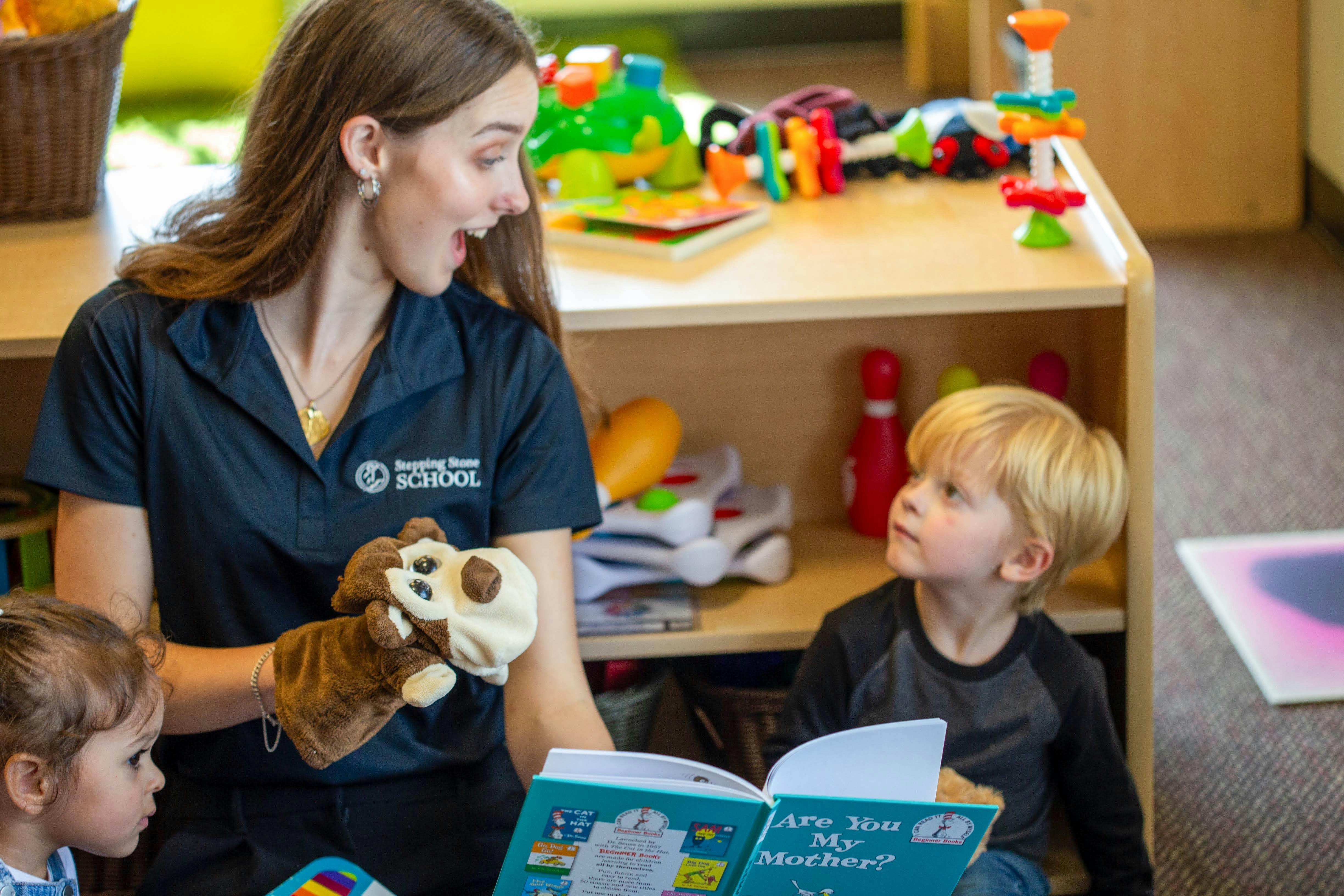 Person holding a puppet and open book in front of two children