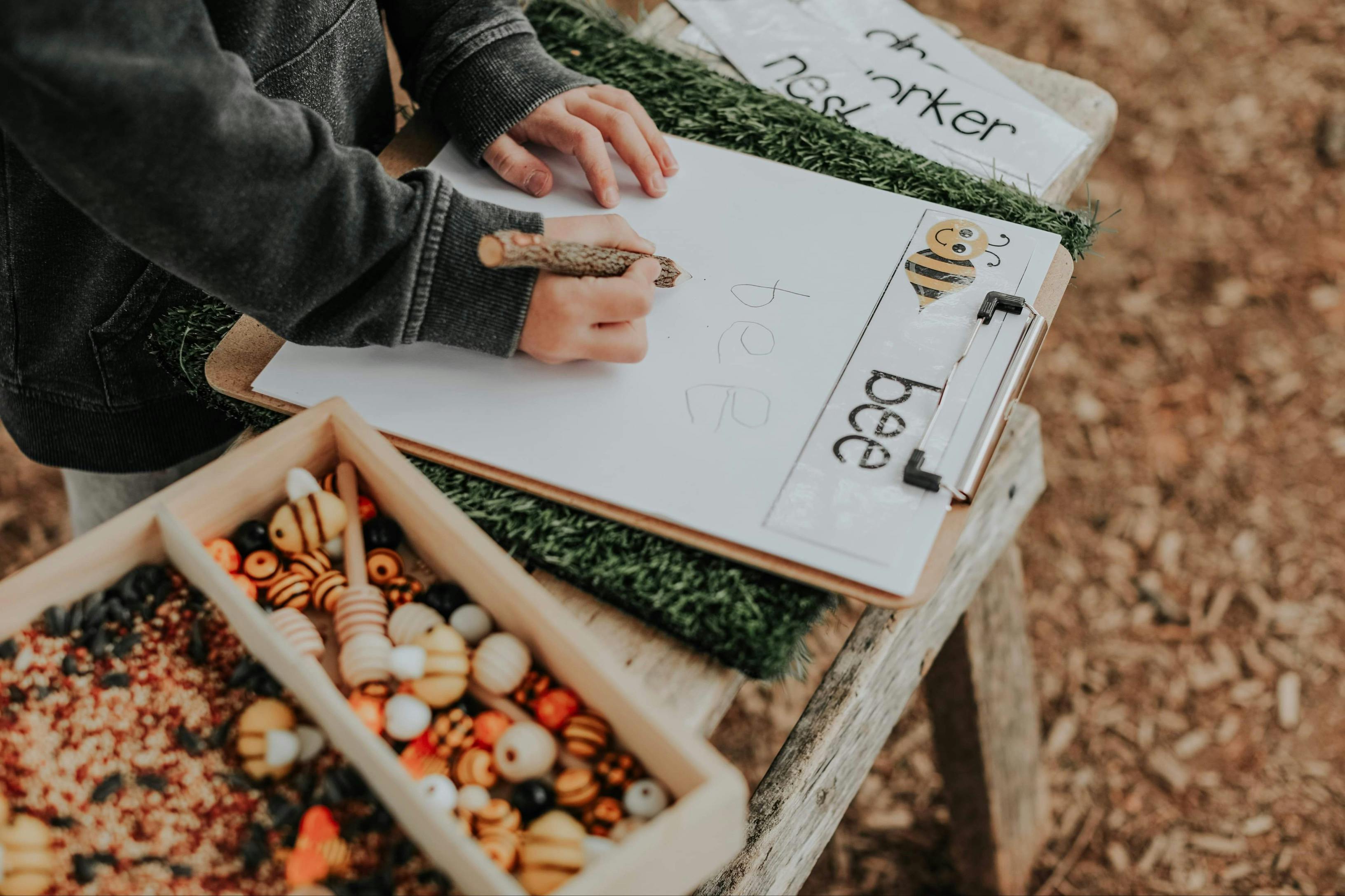 Child writing on a clipboard with a bee illustration