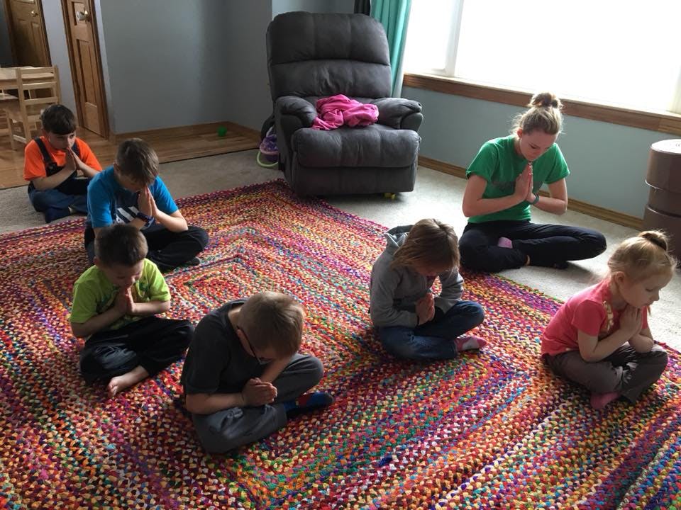 Adult and children sitting on a rug with hands together