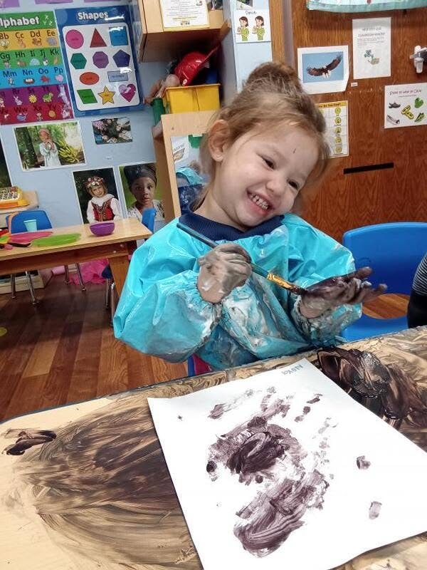 Child wearing a smock painting with dark paint in a classroom