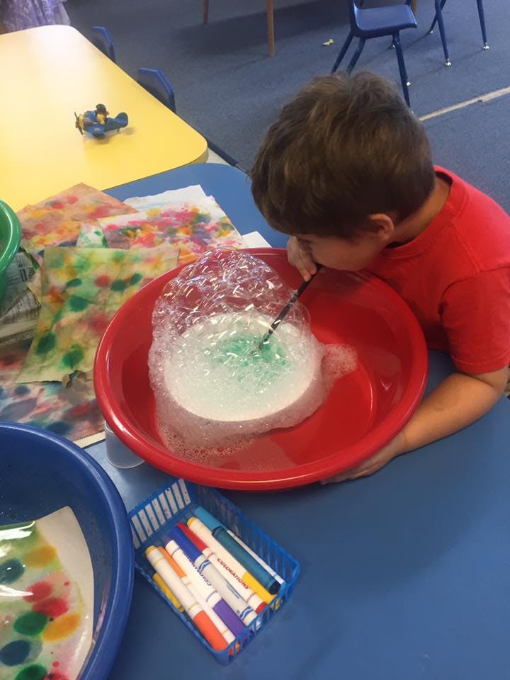 Child blowing bubbles into a red bowl with a straw