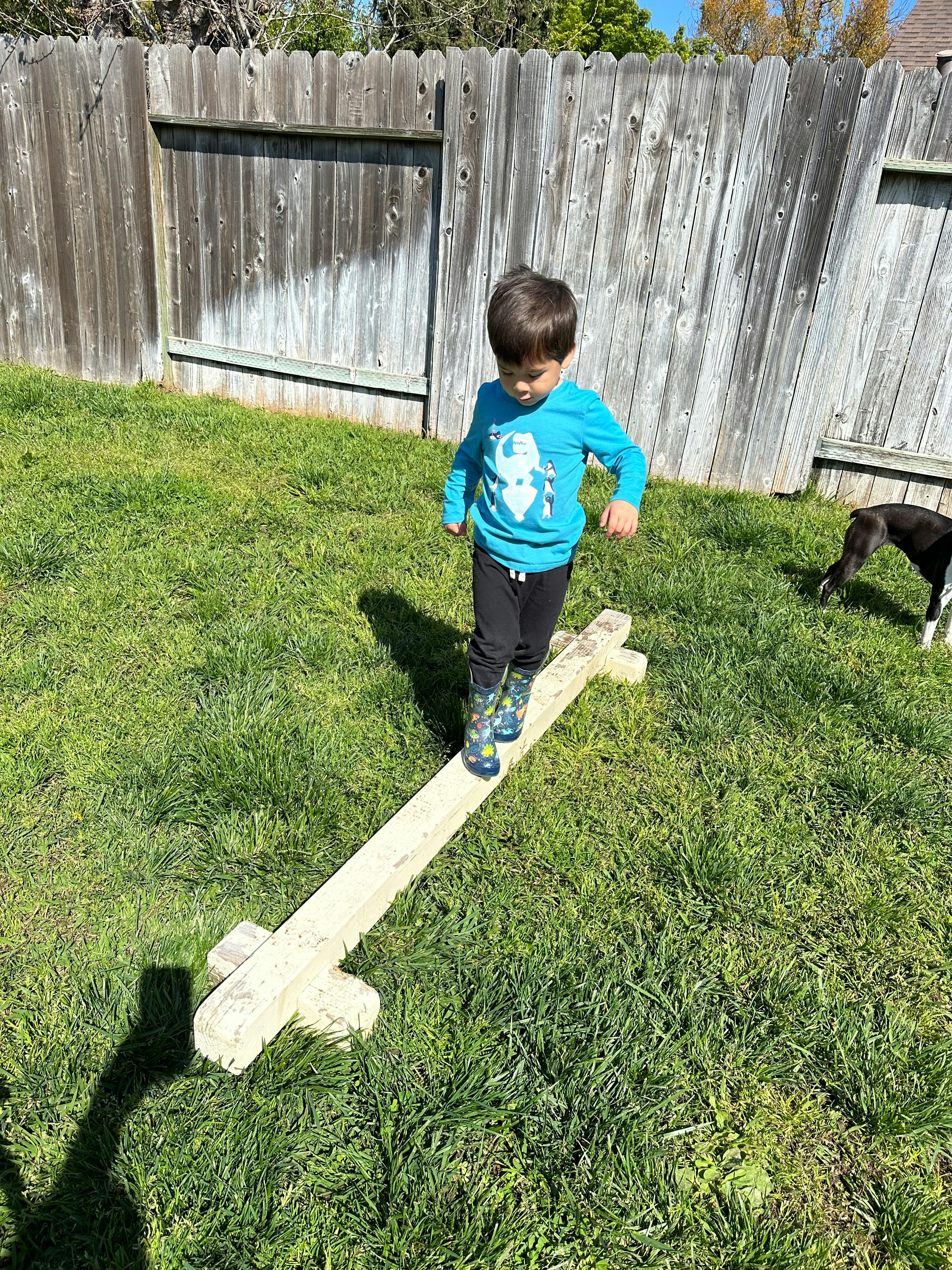 Child walking on a balance beam in a grassy yard