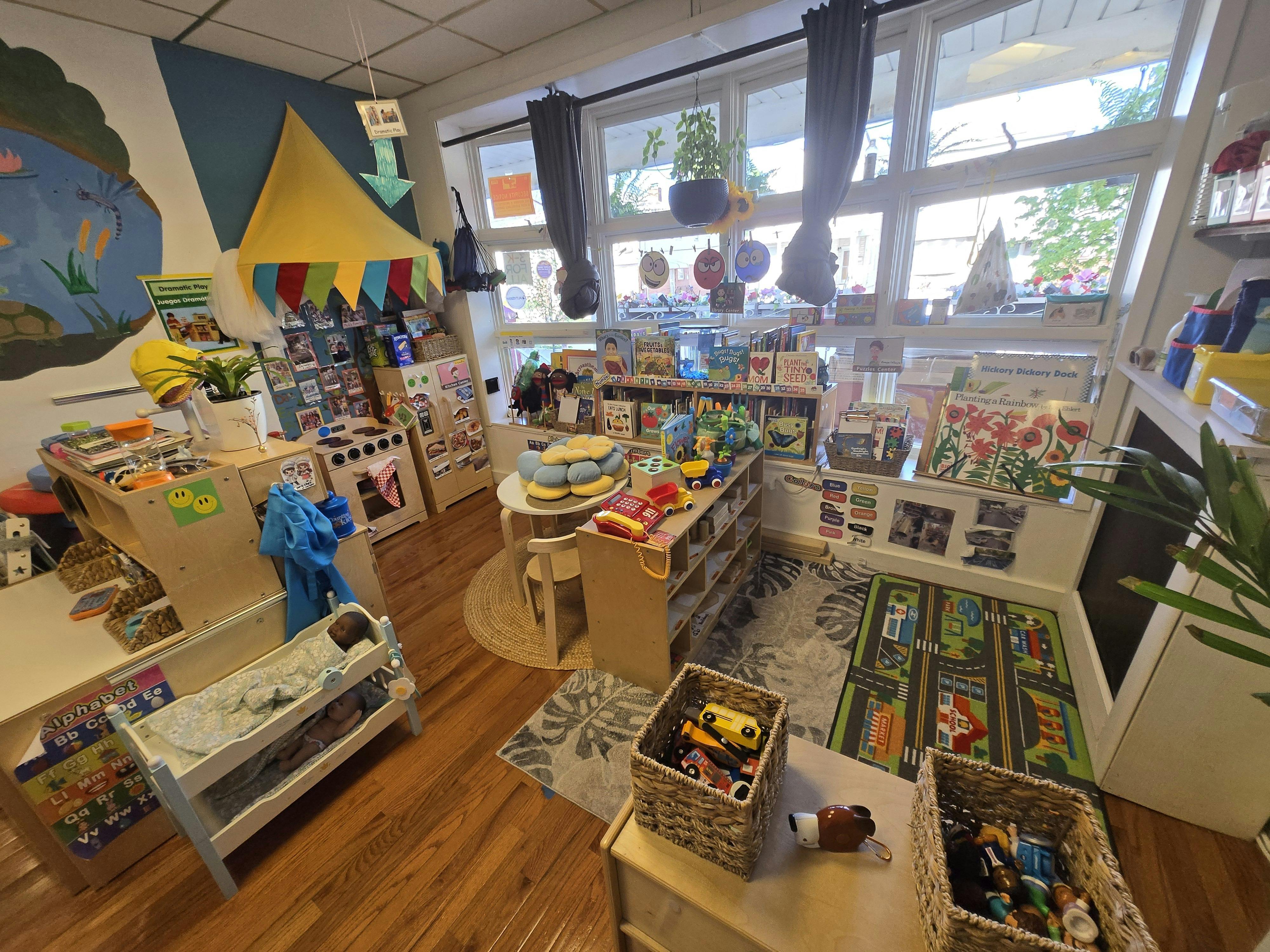 Colorful classroom with play kitchen, toy beds, children's books, and a patterned rug