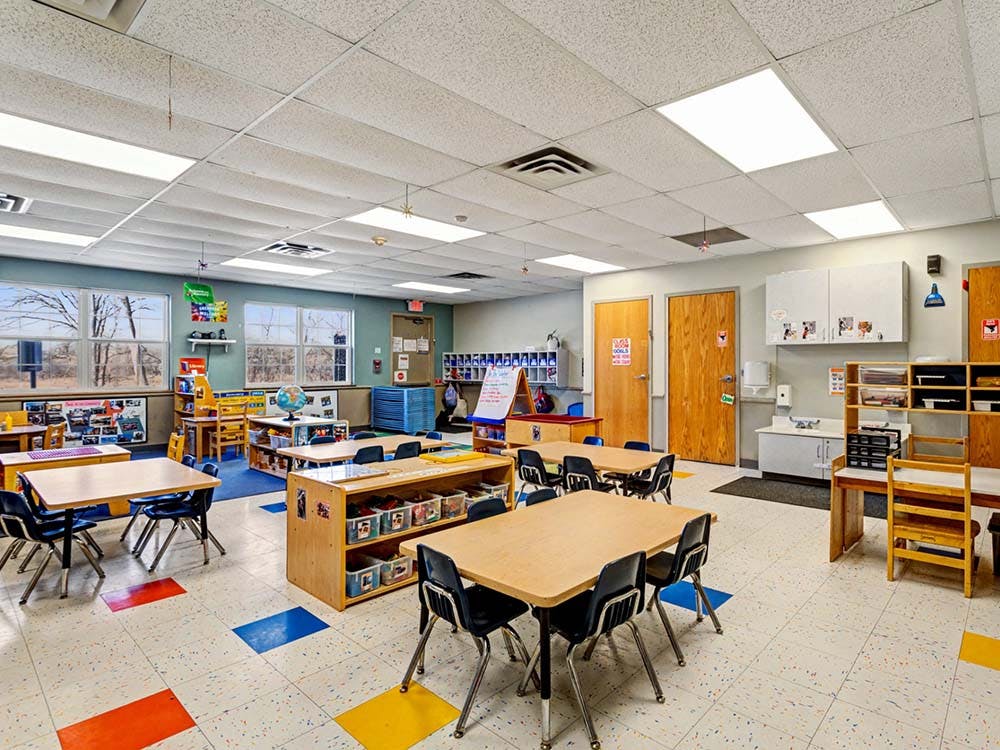 Empty classroom with small tables and chairs, storage units, and windows