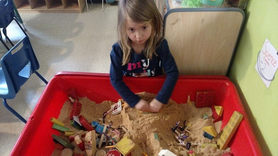 Child playing in a red sand table with toys