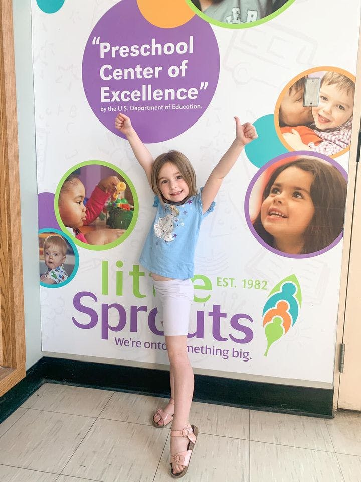 Child standing in front of a wall with text "Preschool Center of Excellence"