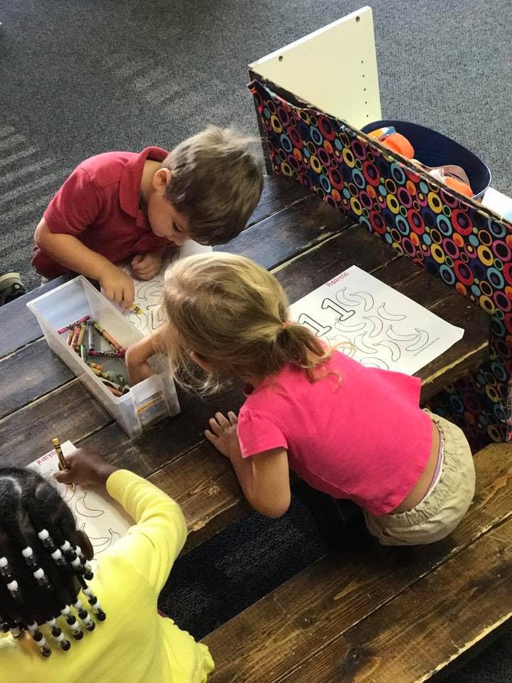 Three children coloring at a wooden table