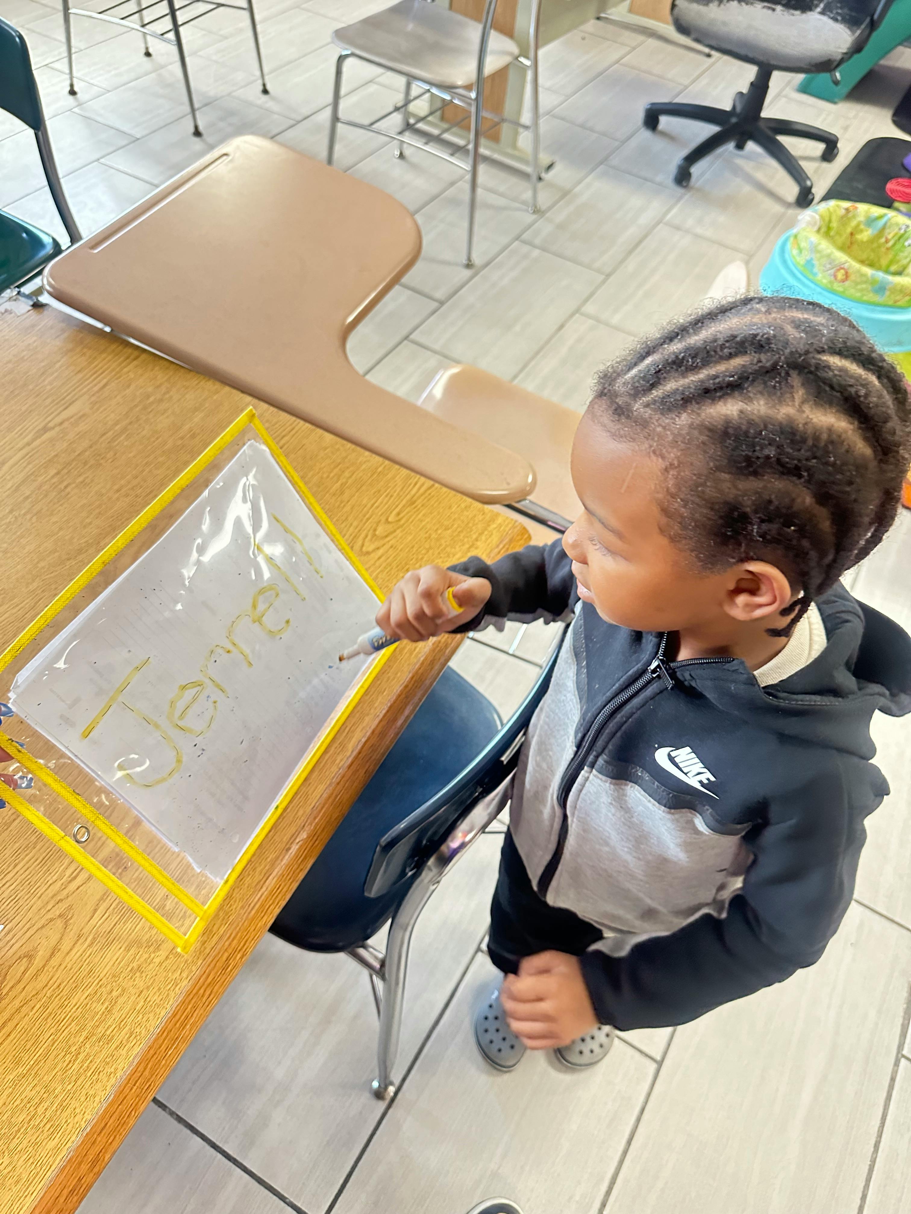Child writing on a clear plastic sheet with a marker in a classroom