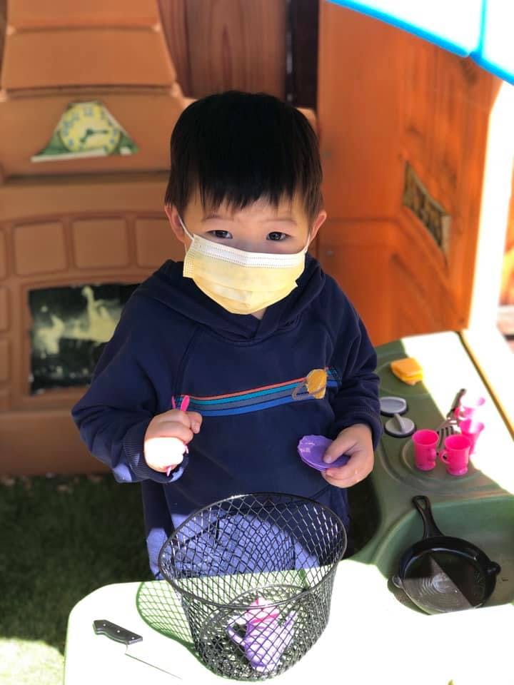 Child in a face mask holding toys next to a play kitchen