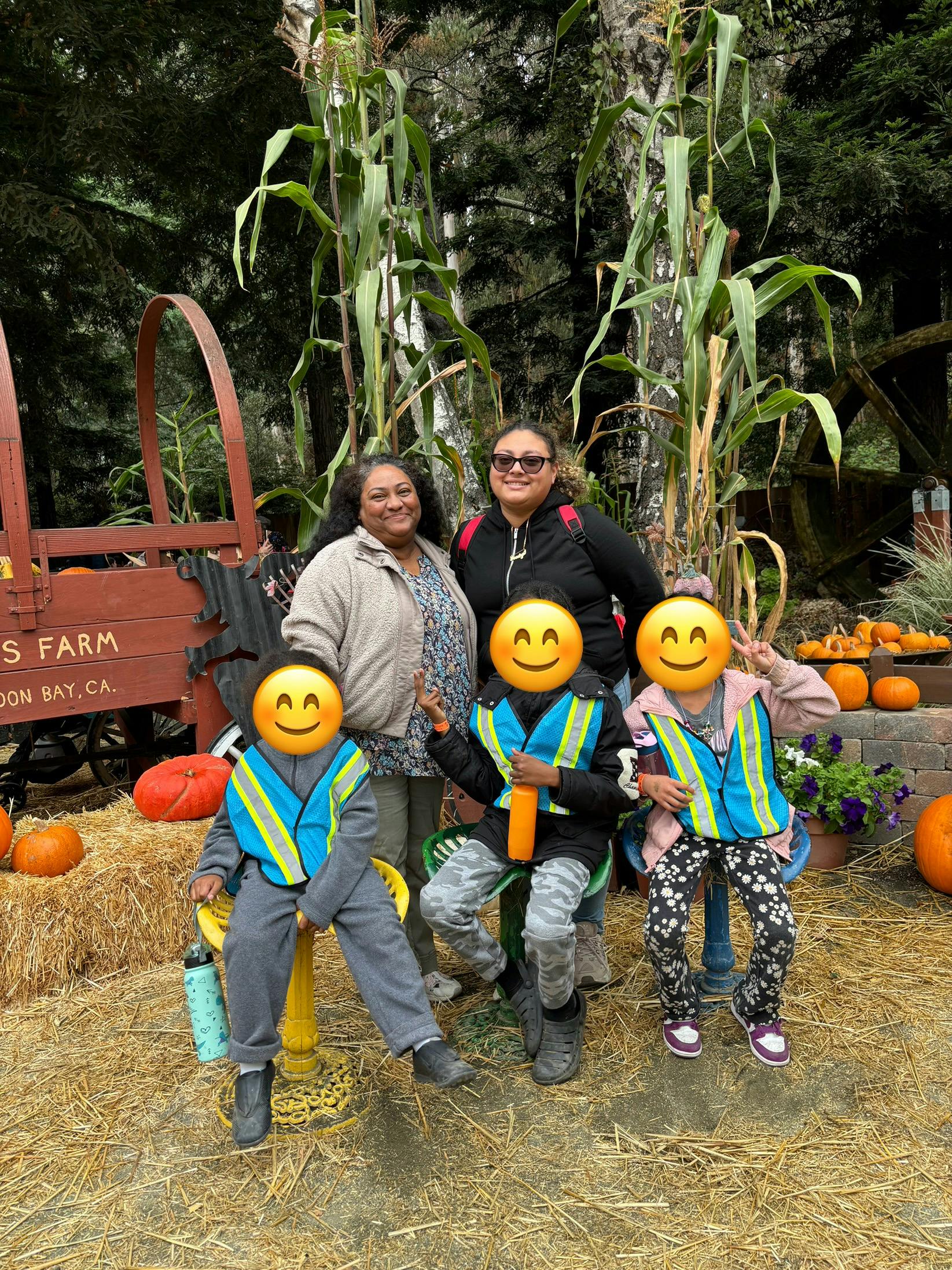 Two adults and three children posing in front of corn stalks and pumpkins