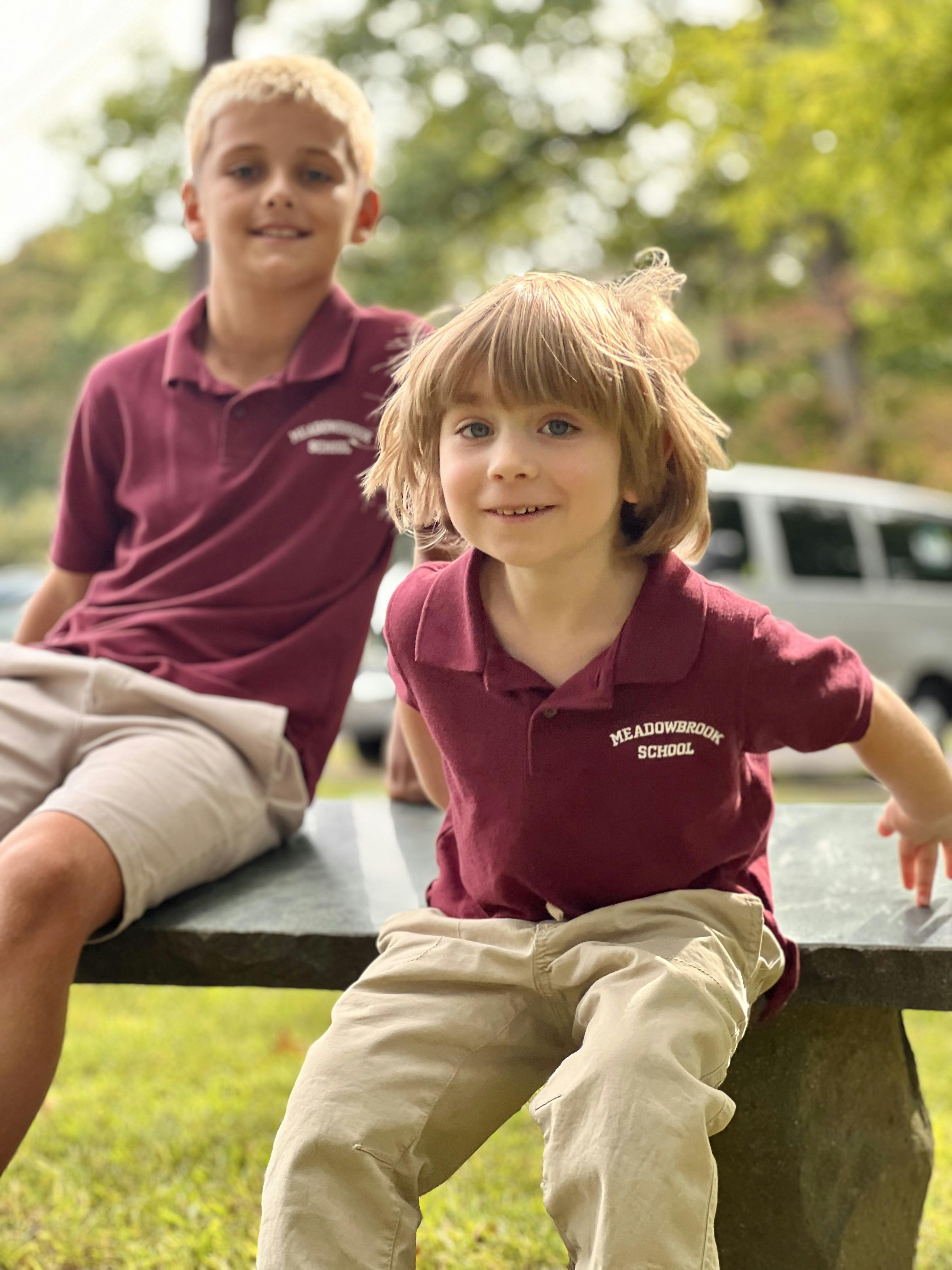 Two children wearing Meadowbrook School uniforms sitting on an outdoor bench
