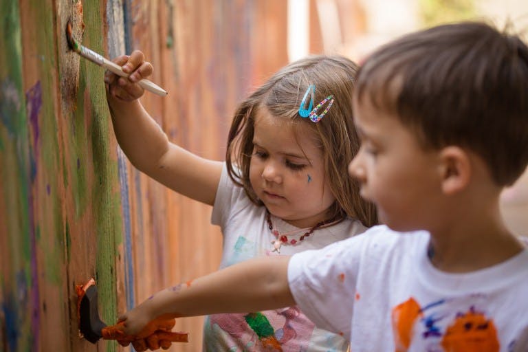 Two children painting on a surface with brushes