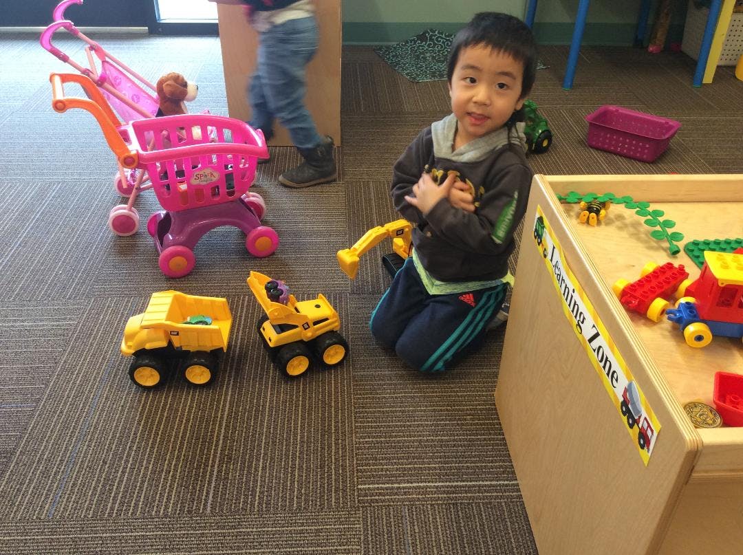 Child kneeling on carpet with toy trucks, Learning Zone text on wooden furniture