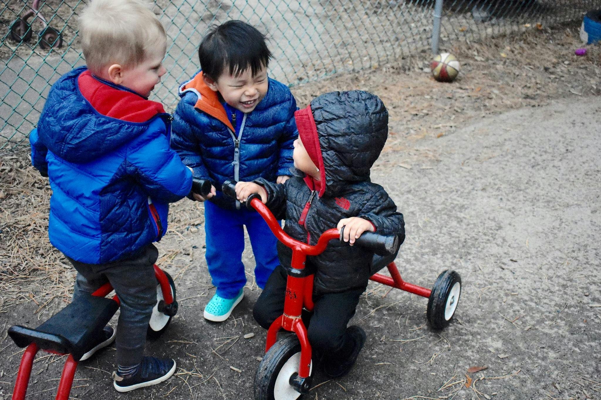 Three children playing with tricycles outdoors