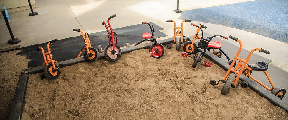 Several small tricycles and scooters in a sandbox