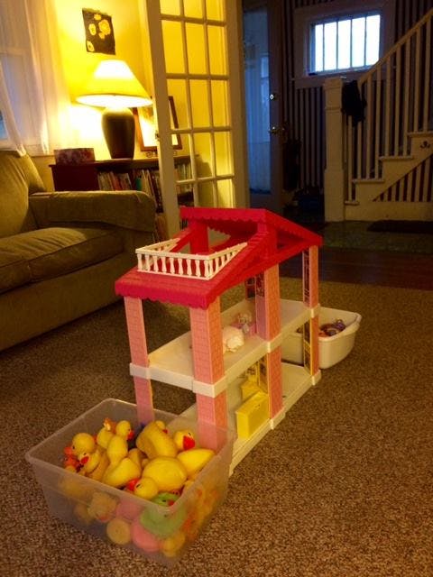 Pink and white toy dollhouse with a bin of rubber ducks