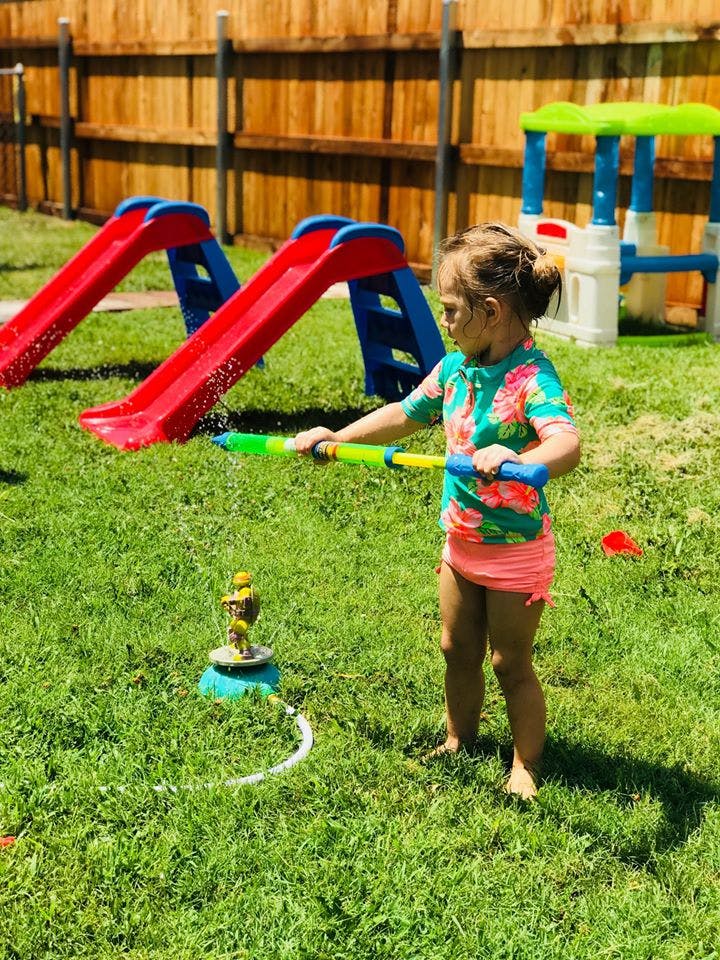 Child holding a water gun in a grassy yard with slides