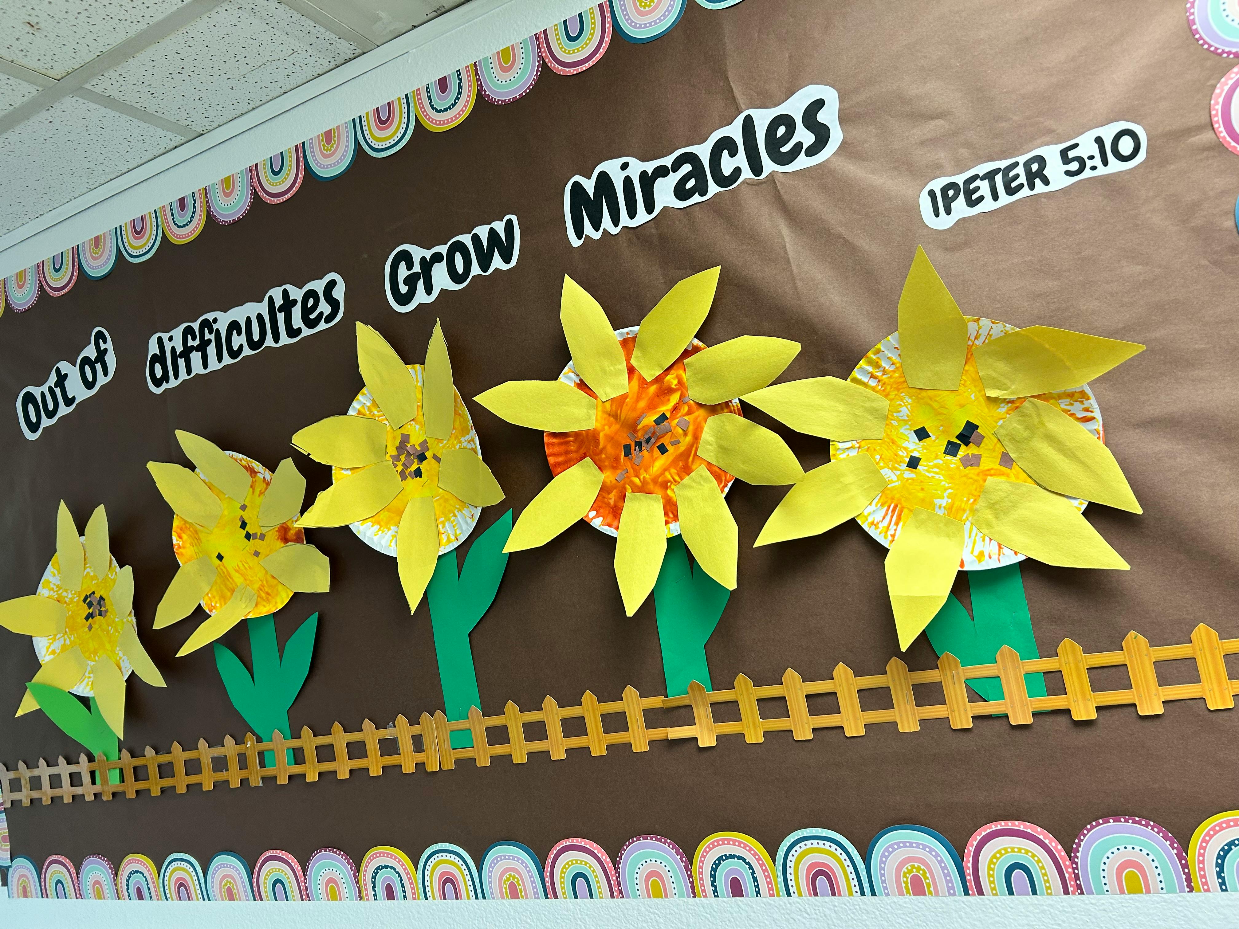 Bulletin board with paper flowers and text "Out of difficulties Grow Miracles"