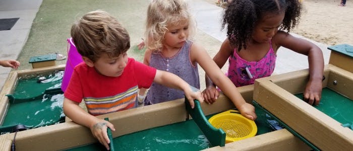 Three children playing with water in a water table