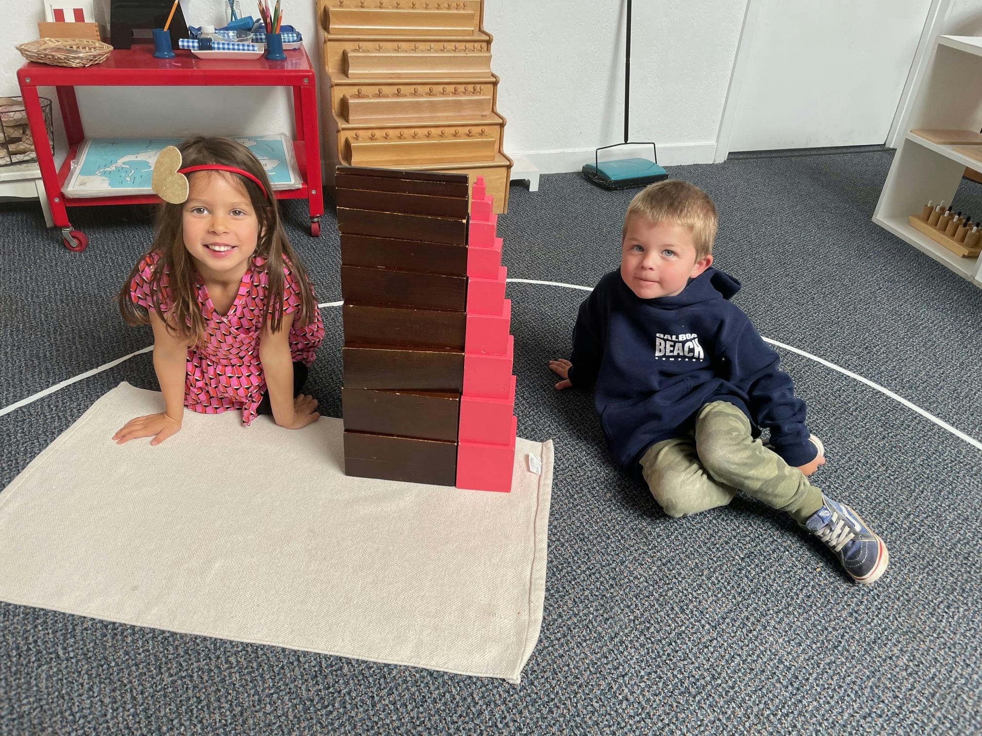 Two children sitting on the floor next to a tall block tower