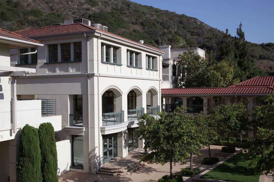 White building with arched balconies and red tile roofs against a hillside