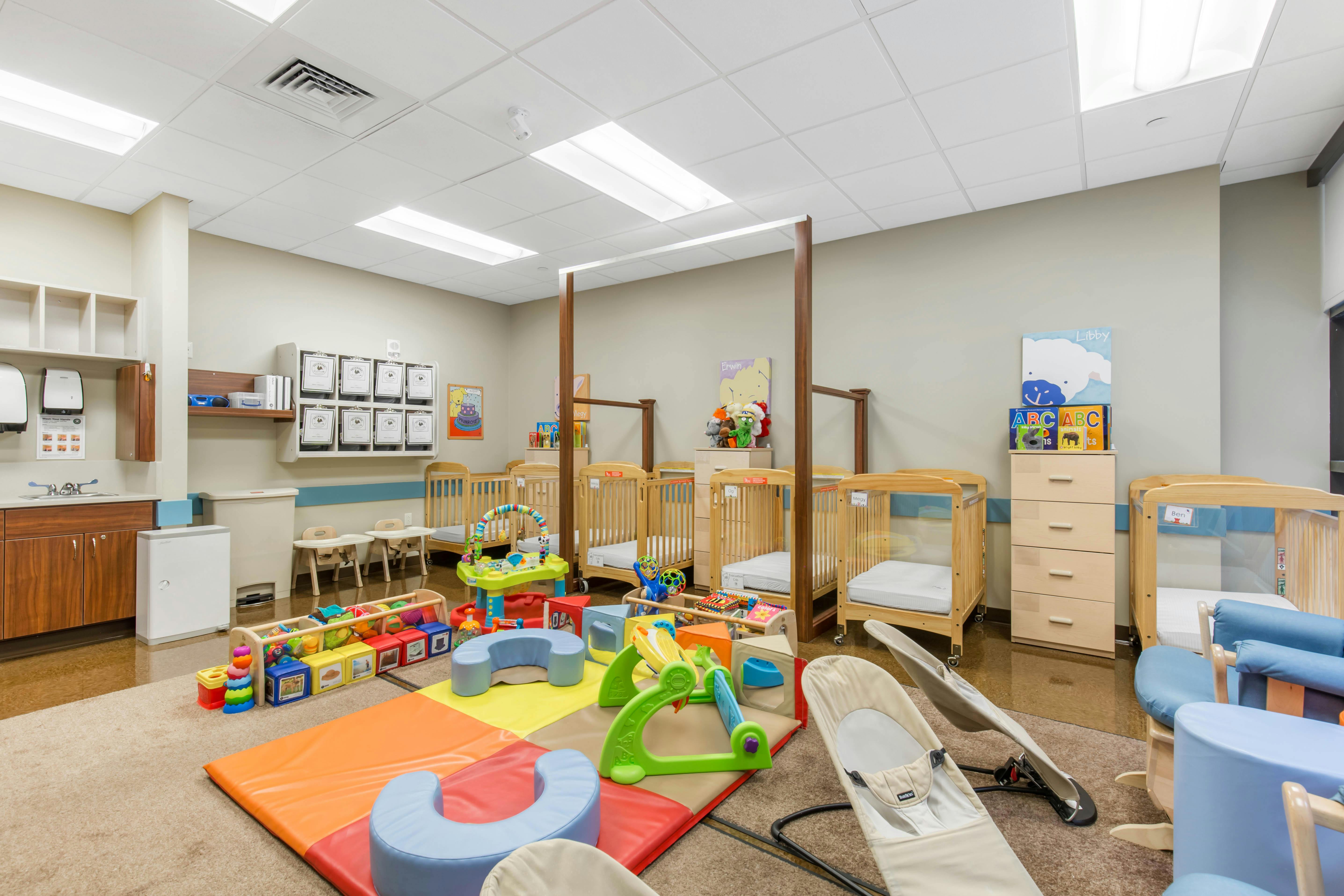 Several baby cribs, playmats, and toys in a bright room