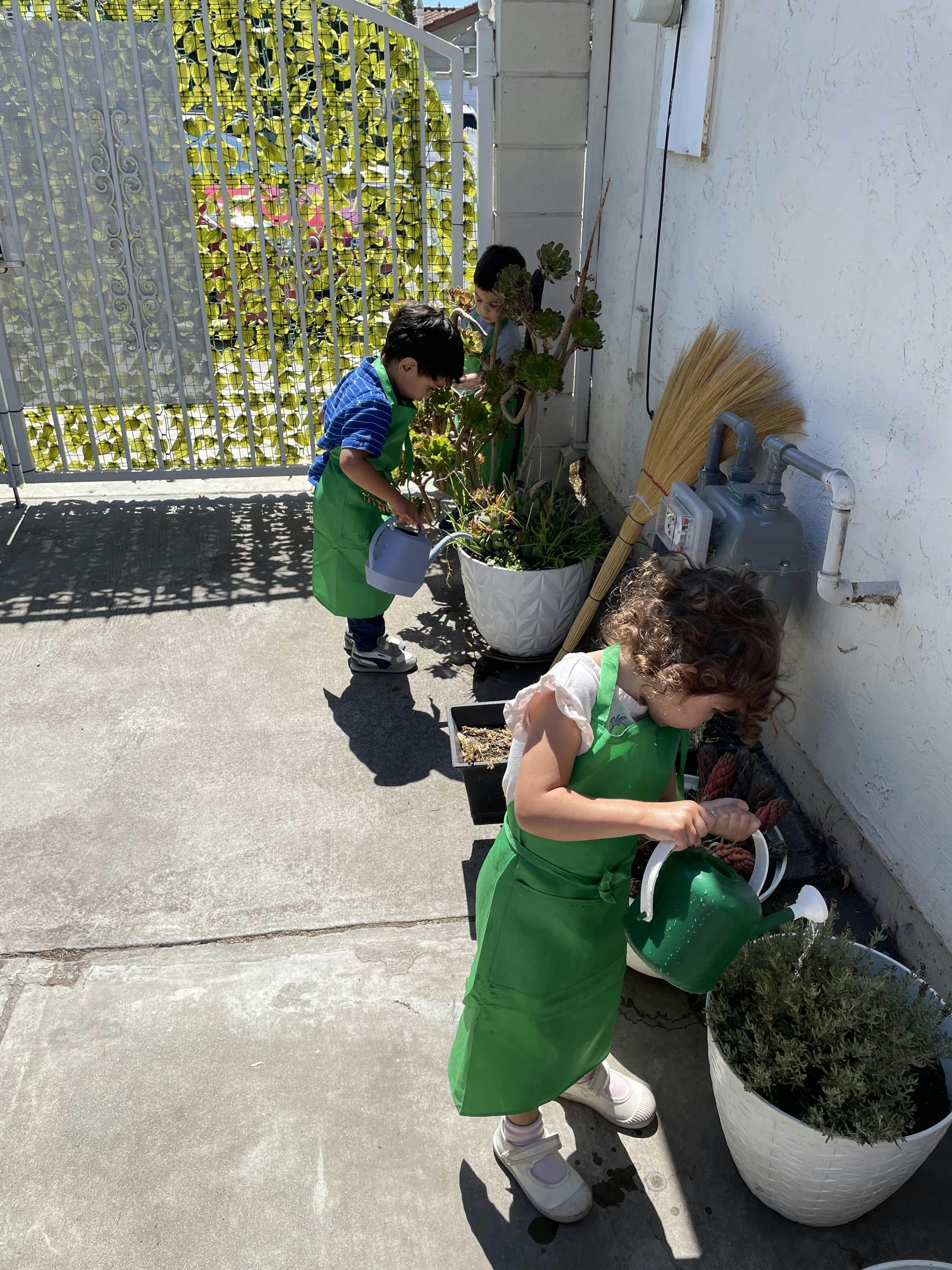 Children in aprons watering plants in pots