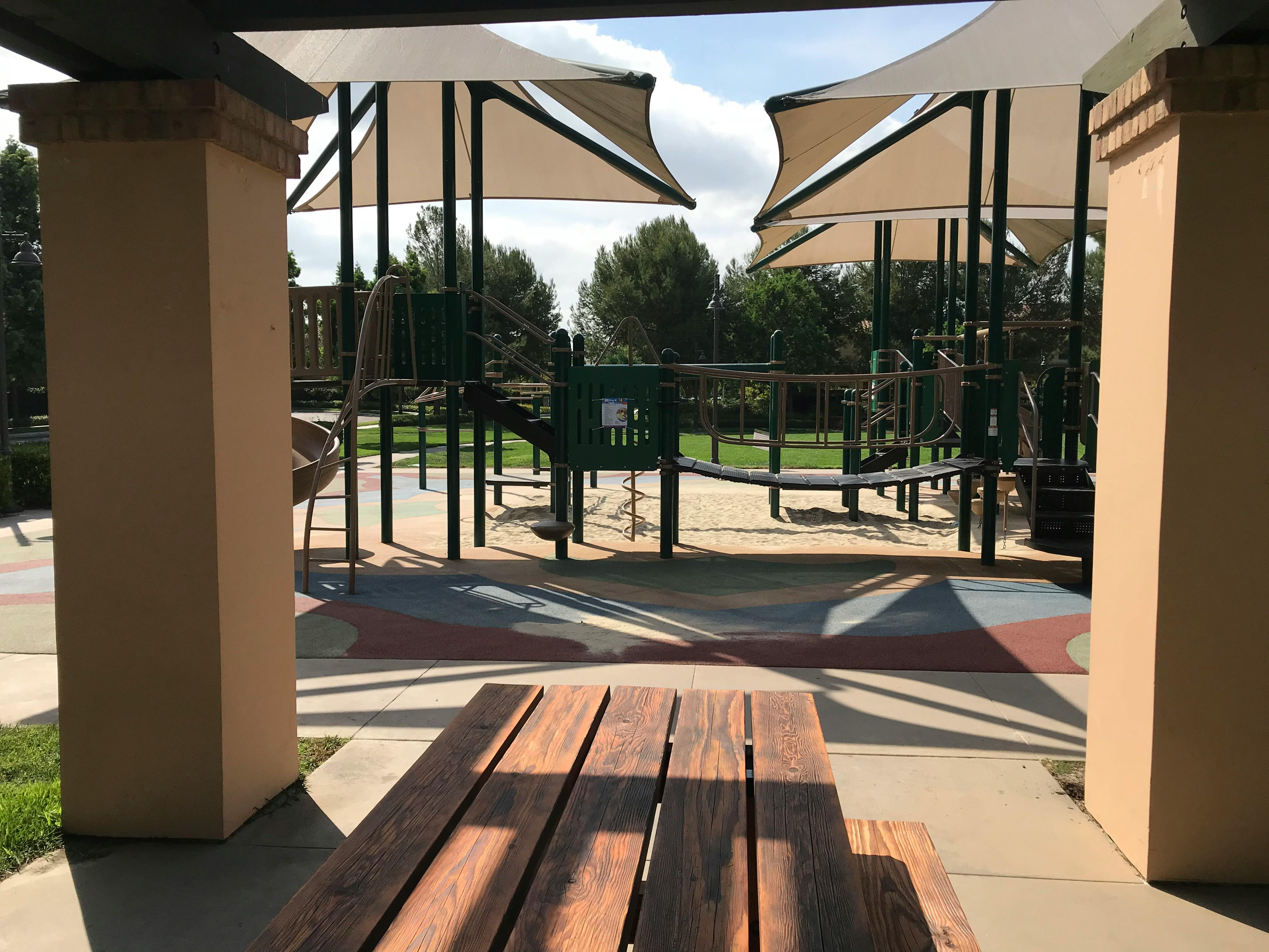Playground with shade structures and a wooden picnic table in the foreground